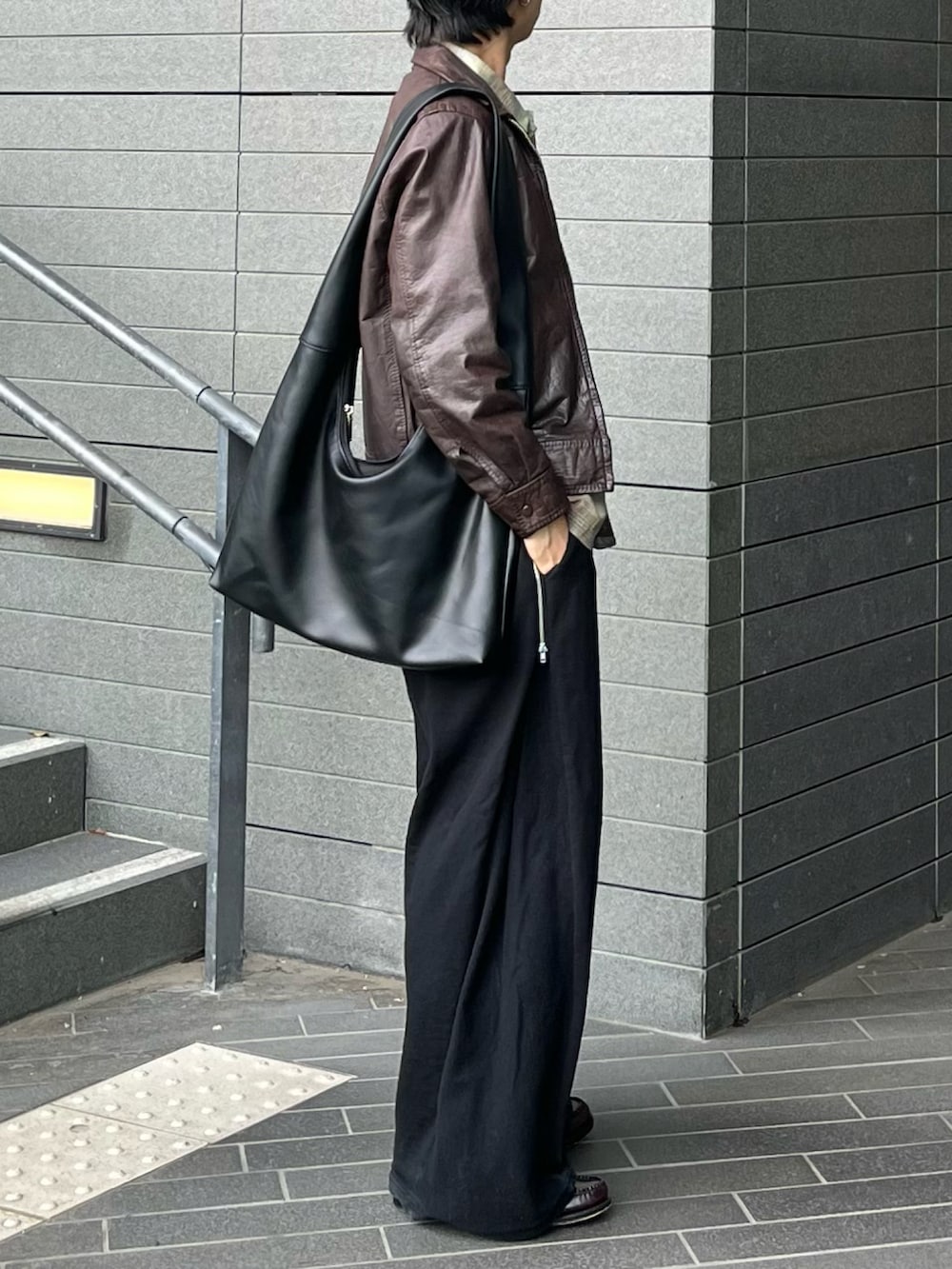 ブラック系のスウェットパンツ、ブラック系のショルダーバッグ、ブラウン系のローファーを着用したメンズの春コーディネートの2枚目の写真