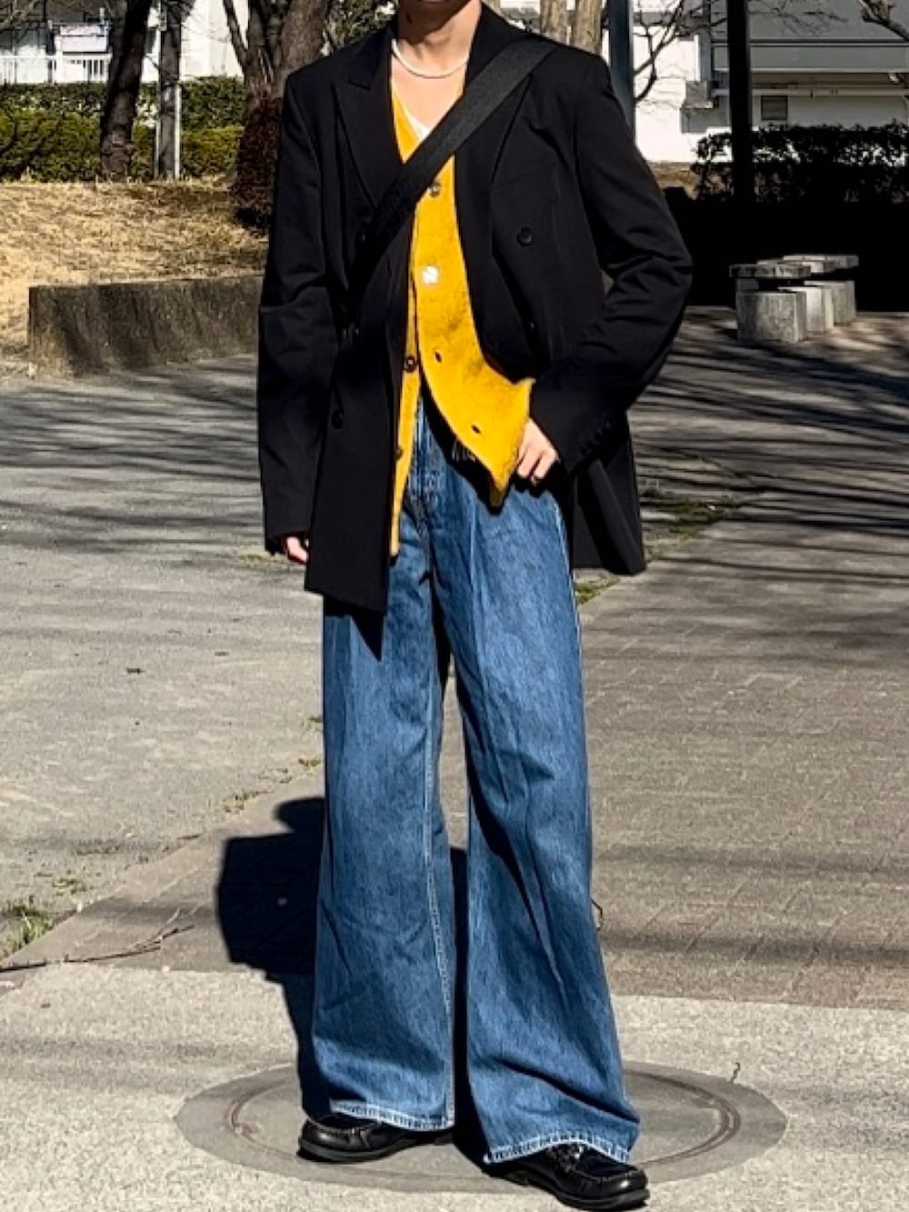 イエロー系のカーディガン/ボレロ、ブラック系のテーラードジャケット、ブルー系のデニムパンツを着用したメンズの春コーディネートの2枚目の写真