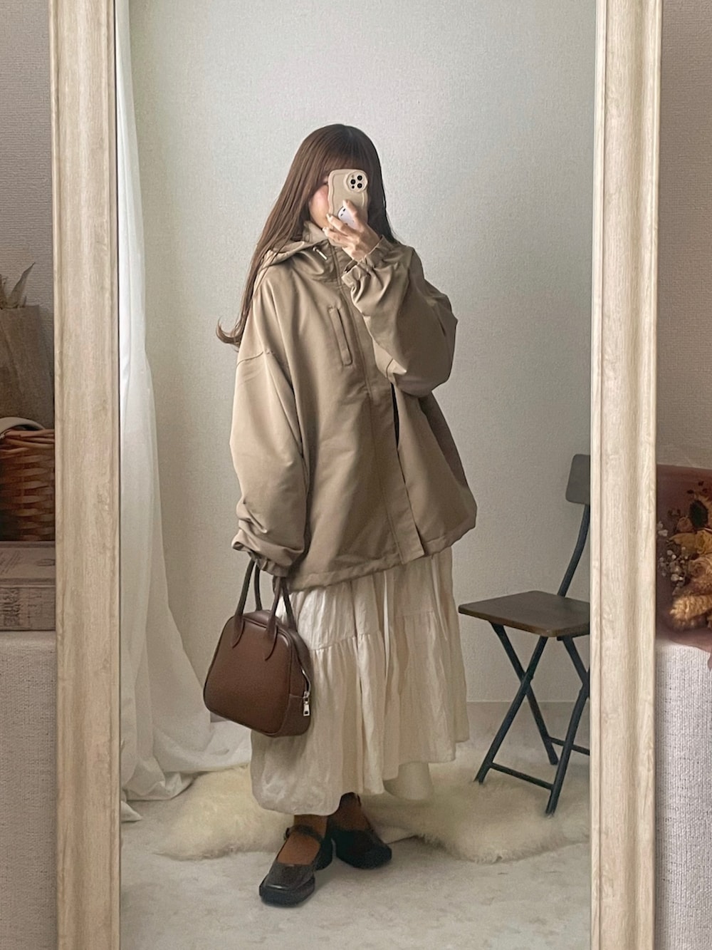 ベージュ系のマウンテンパーカー、ブラウン系のボストンバッグ、ホワイト系のワンピースを着用したレディースの冬コーディネートの2枚目の写真