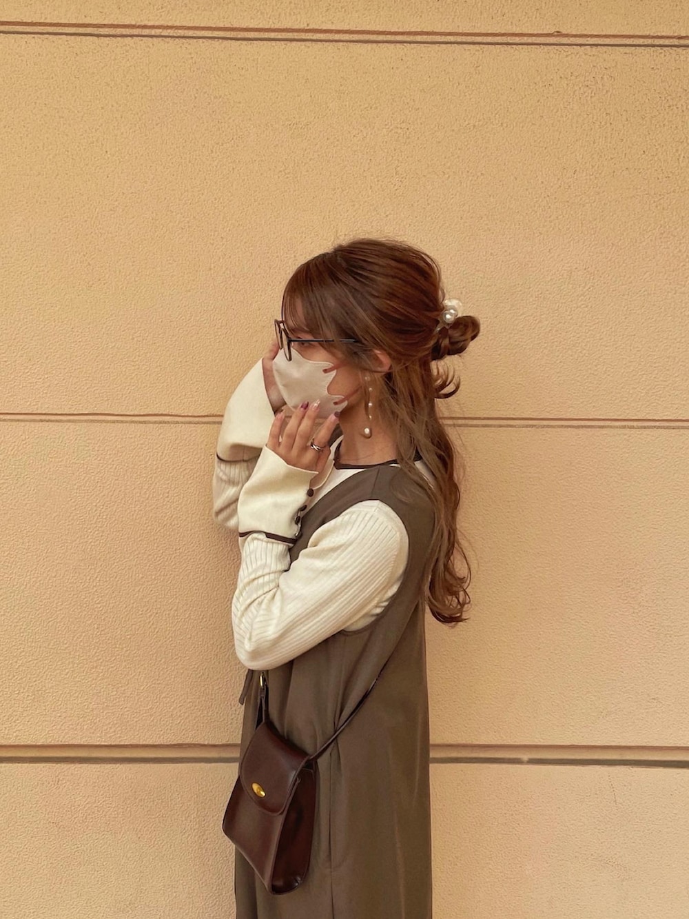 ブラウン系のジャンパースカート、ホワイト系のニット/セーター、ブラウン系のショルダーバッグを着用したレディースの秋コーディネートの2枚目の写真