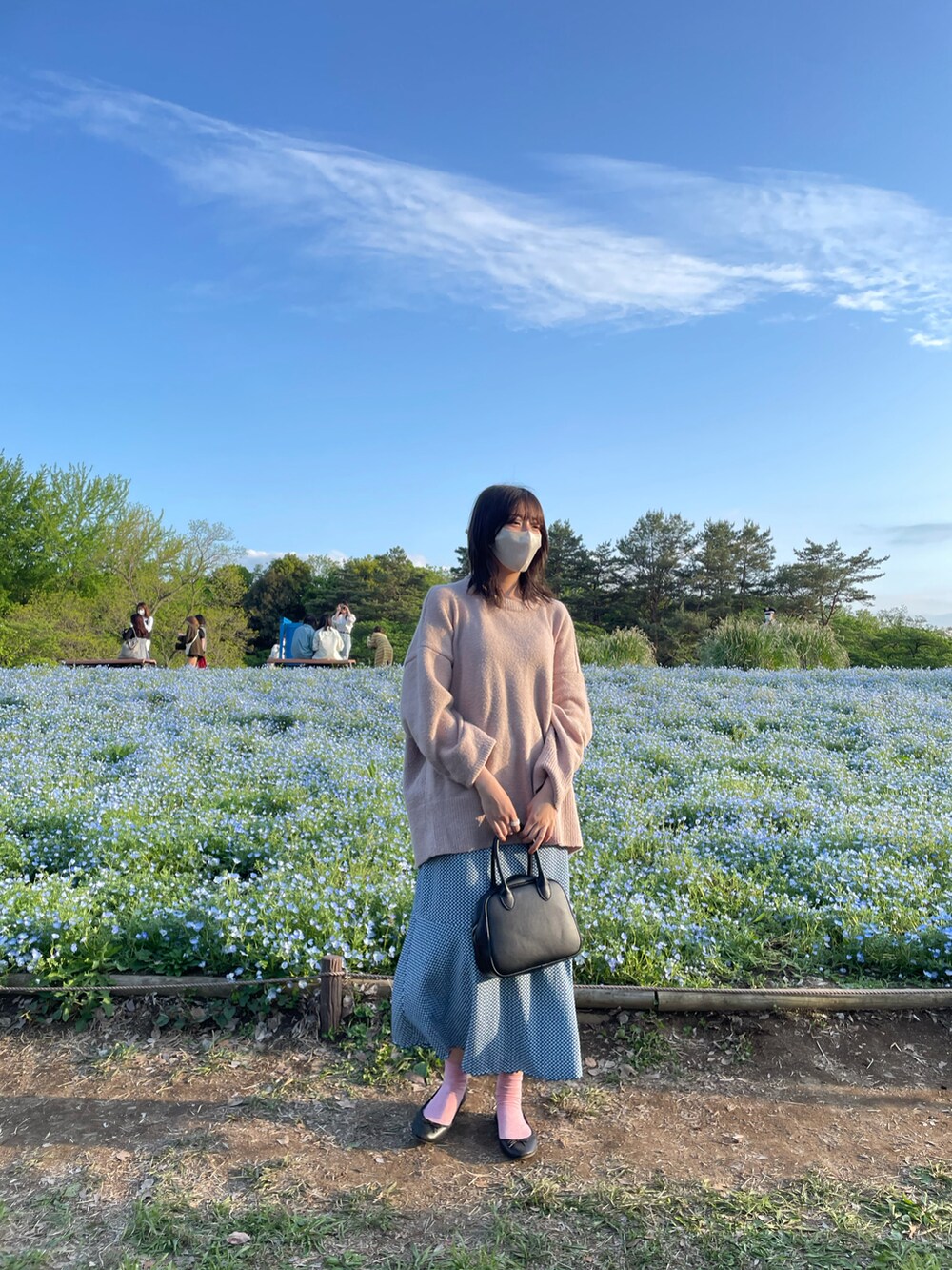 ピンク系のニット/セーター、ブルー系のスカート、ブラック系のトートバッグを着用したレディースの春コーディネートの2枚目の写真