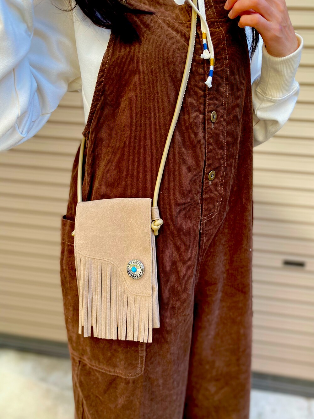 ホワイト系のパーカー、ベージュ系のショルダーバッグ、ブラウン系のサロペット/オーバーオールを着用したレディースの秋コーディネートの4枚目の写真