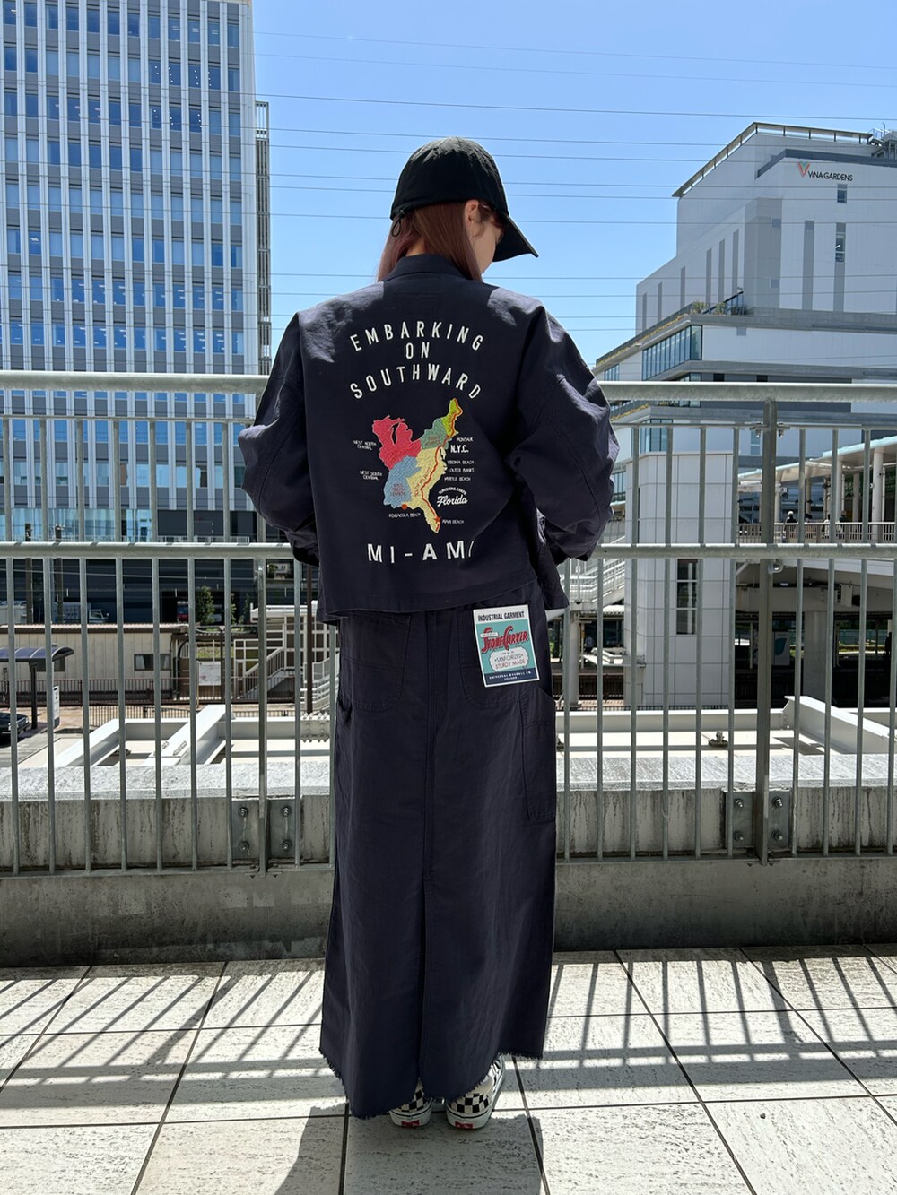 ブルー系のカバーオール、ブルー系のスカート、ブラック系のキャップを着用したレディースの春コーディネートの2枚目の写真