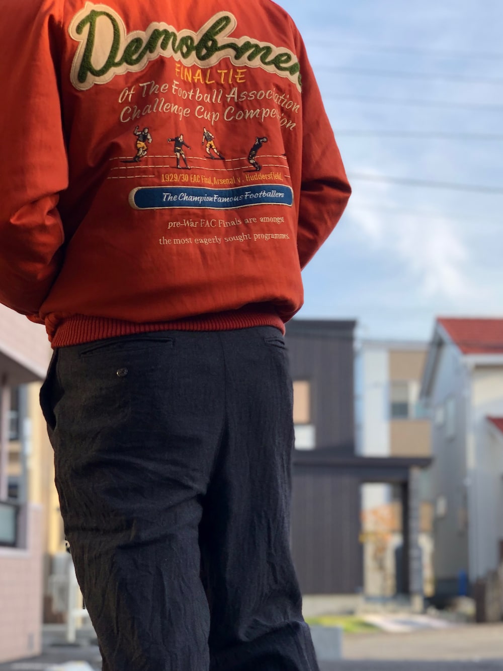 オレンジ系のスタジャン、ブラック系のスラックス、ブラック系のドレスシューズを着用したメンズの秋コーディネートの2枚目の写真