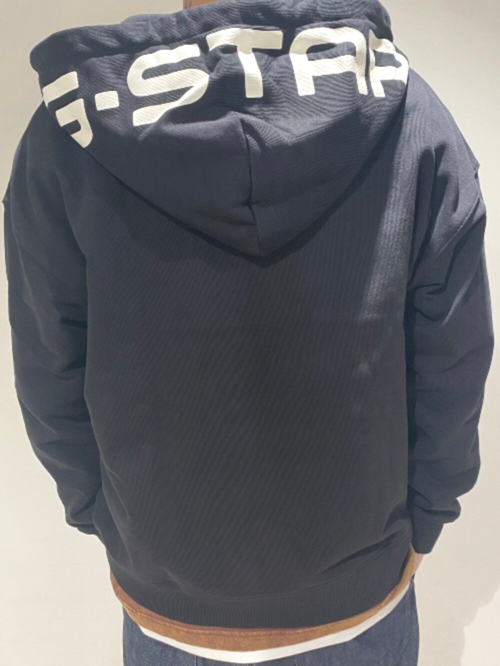 ブラック系のパーカー、ブラウン系のTシャツ/カットソー、ブルー系のデニムパンツを着用したメンズの秋コーディネートの2枚目の写真