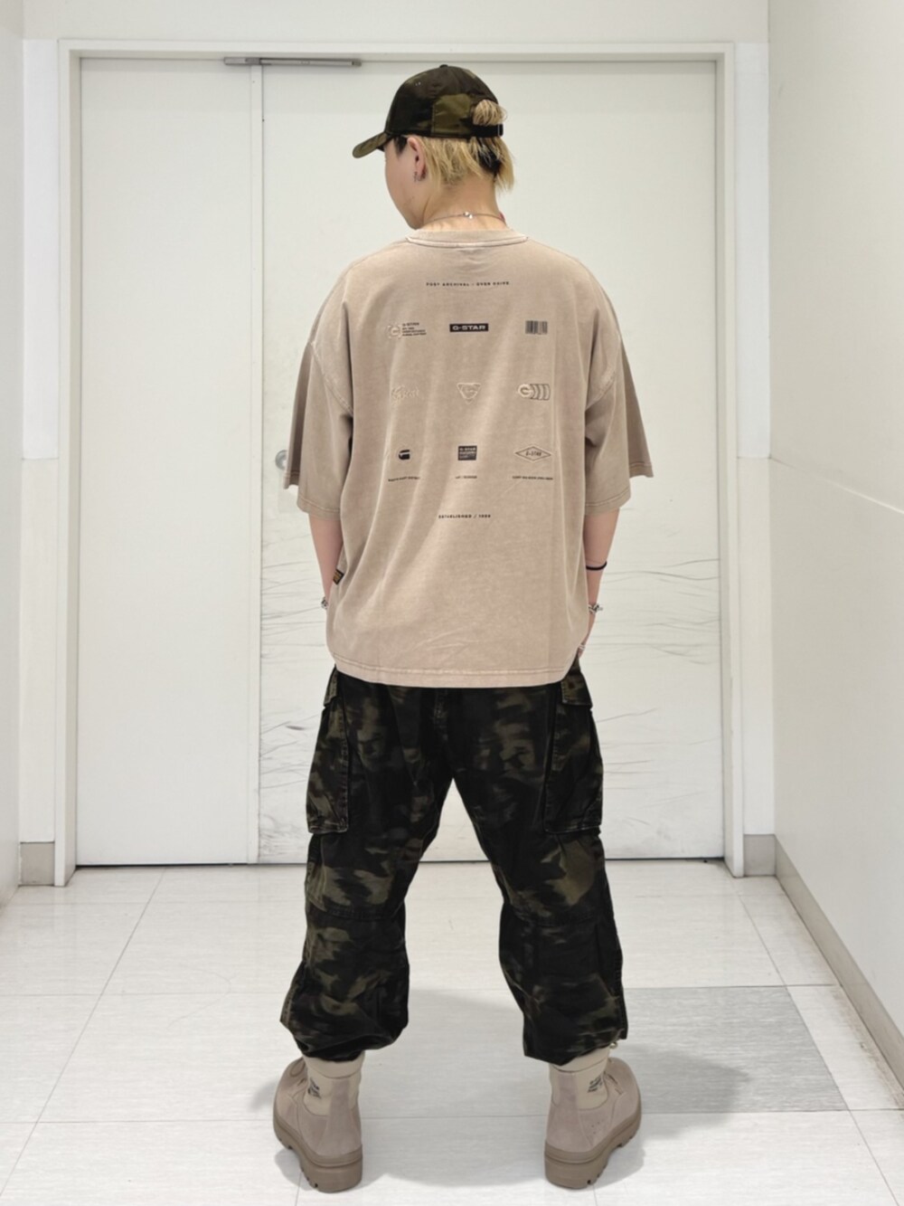 ベージュ系のTシャツ/カットソー、グリーン系のカーゴパンツ、ブラウン系のキャップを着用したメンズの秋コーディネートの2枚目の写真