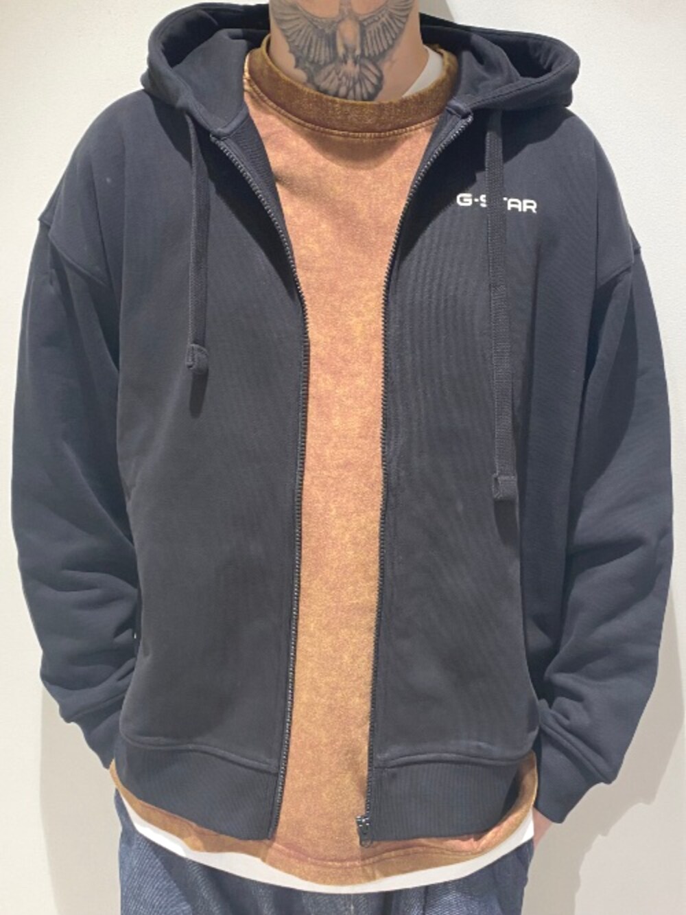 ブラック系のパーカー、ブラウン系のTシャツ/カットソー、ブルー系のデニムパンツを着用したメンズの秋コーディネートの3枚目の写真