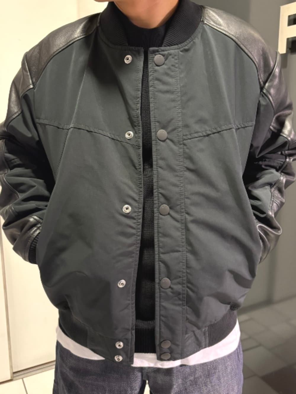 ブラック系のスタジャン、ブラック系のニット/セーター、ブルー系のデニムパンツを着用したメンズの秋コーディネートの2枚目の写真