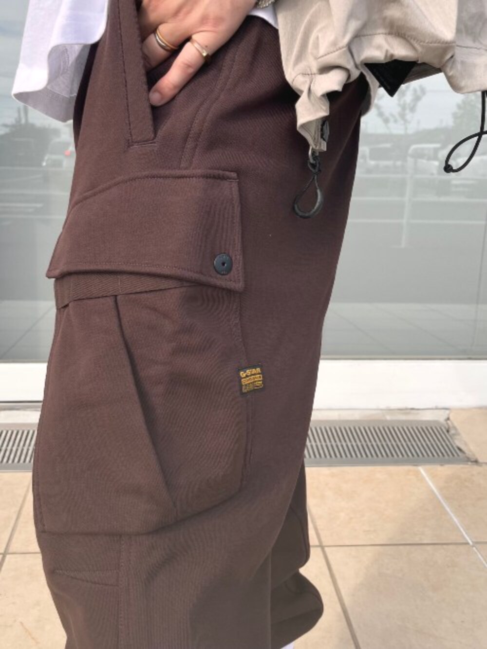 ホワイト系のTシャツ/カットソー、ベージュ系のナイロンジャケット、ブラウン系のスウェットパンツを着用したメンズの夏コーディネートの3枚目の写真