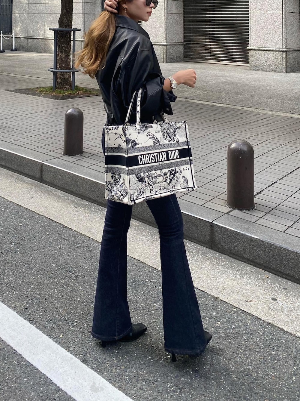 ホワイト系のトートバッグ、ブラック系のライダースジャケット、ブルー系のデニムパンツを着用したレディースの秋コーディネートの4枚目の写真