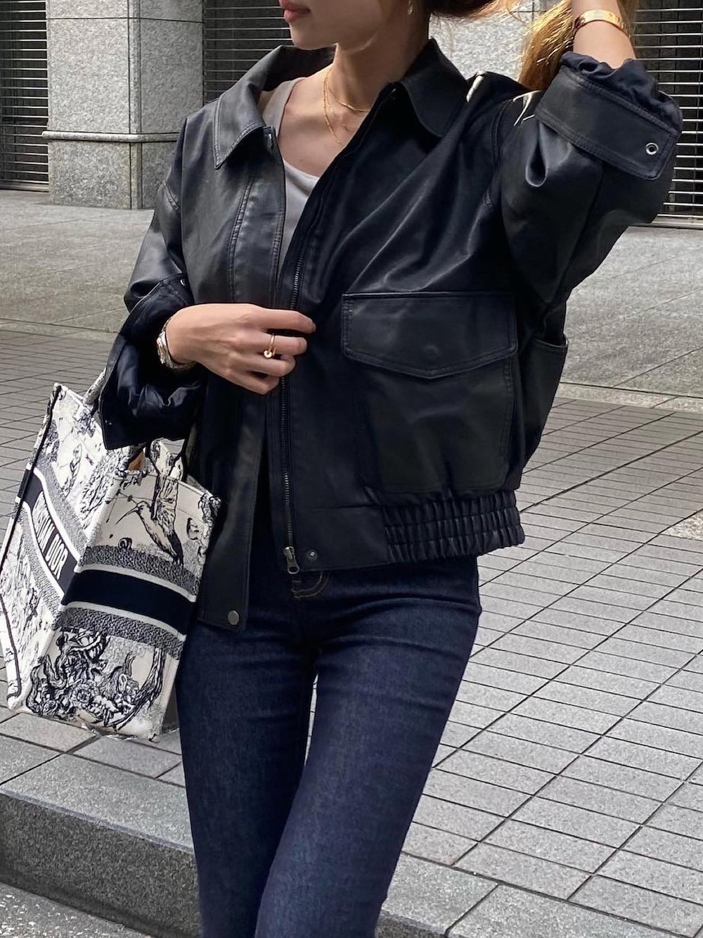 ホワイト系のトートバッグ、ブラック系のライダースジャケット、ブルー系のデニムパンツを着用したレディースの秋コーディネートの5枚目の写真