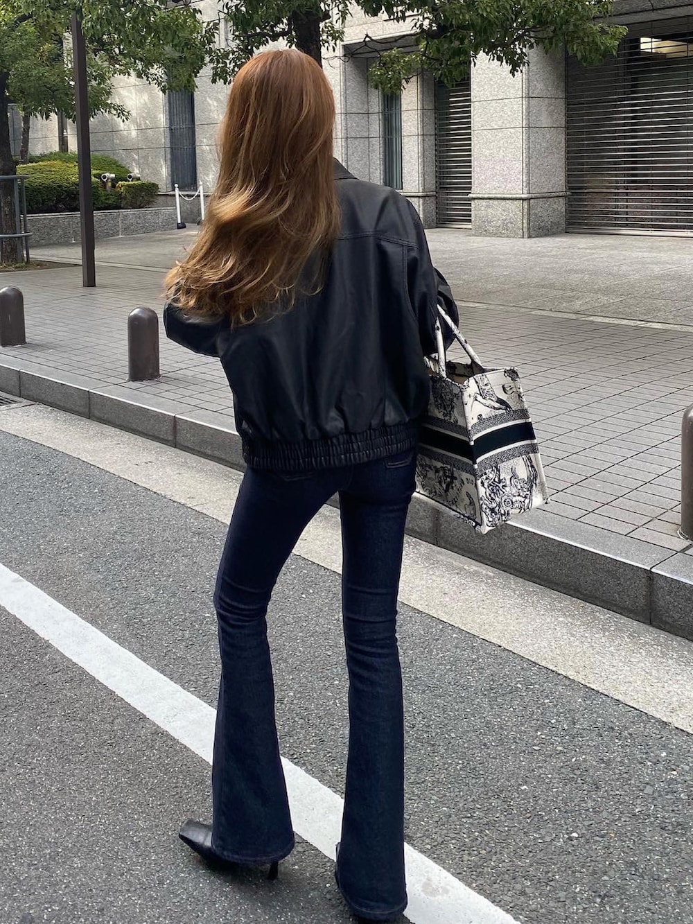 ホワイト系のトートバッグ、ブラック系のライダースジャケット、ブルー系のデニムパンツを着用したレディースの秋コーディネートの2枚目の写真