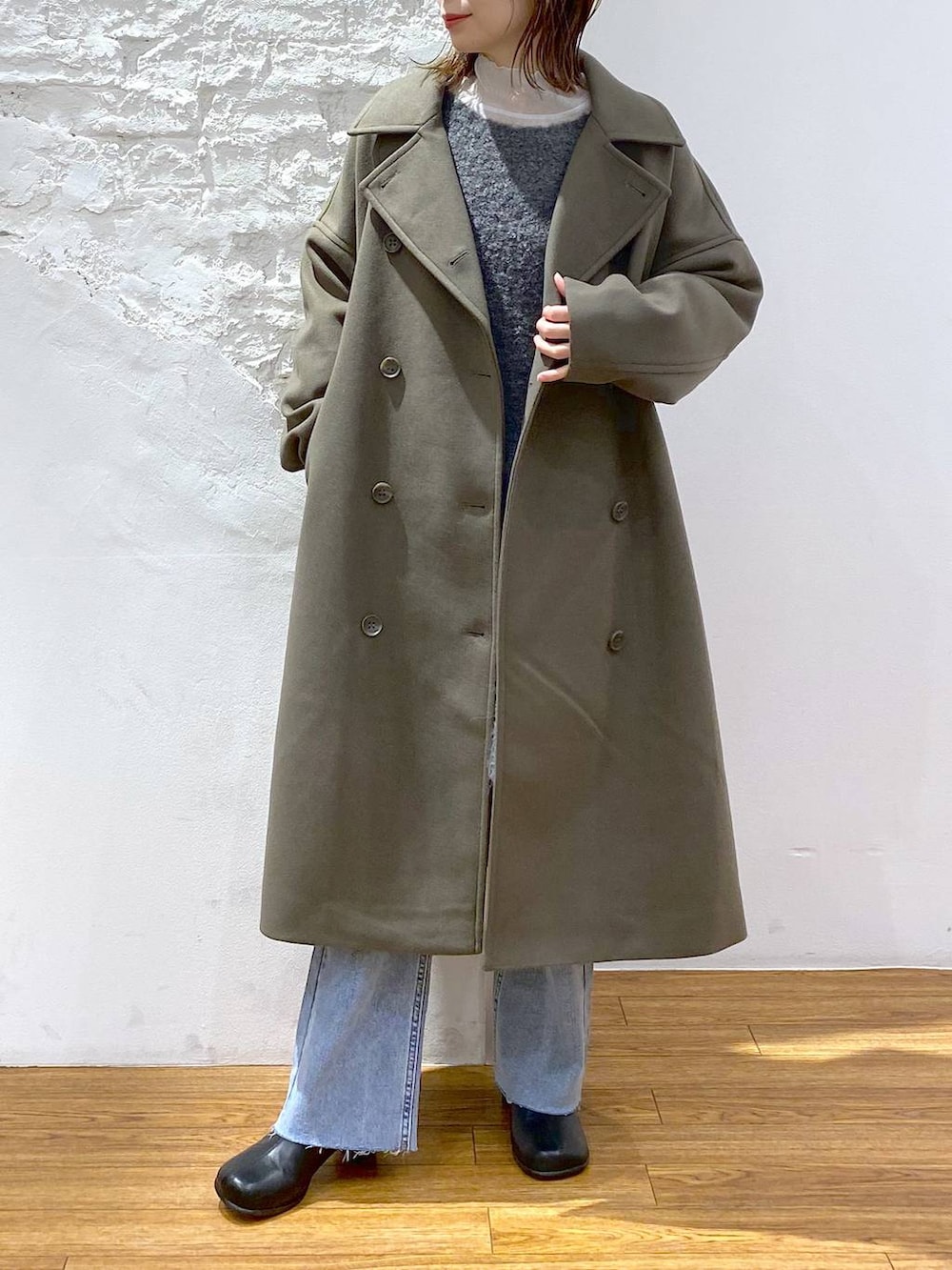 グリーン系のチェスターコート、グレー系のTシャツ/カットソー、ブラック系のブーツを着用したレディースの冬コーディネートの2枚目の写真