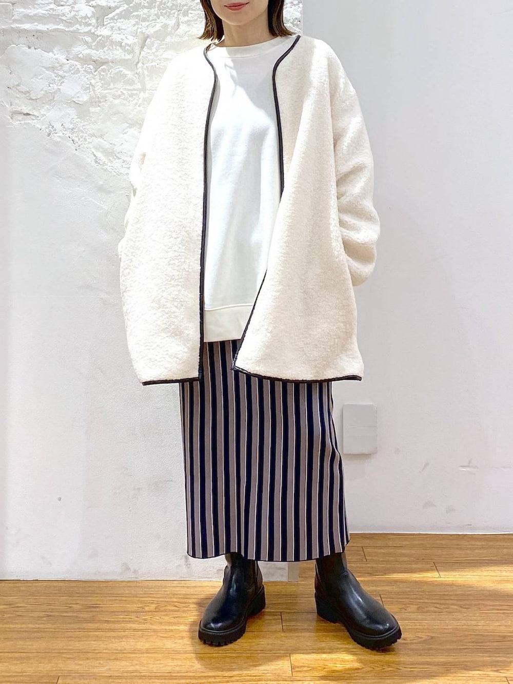 ブラック系のブーツ、ブルー系のスカート、ホワイト系のその他アウターを着用したレディースの冬コーディネートの2枚目の写真