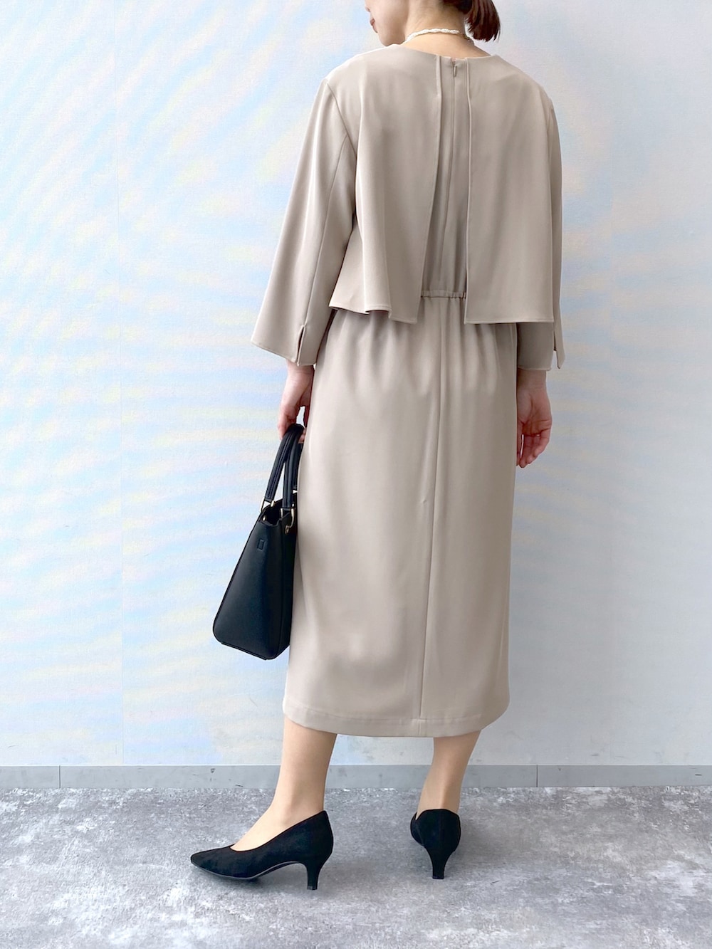 ベージュ系のワンピース、ブラック系のハンドバッグ、ブラック系のパンプスを着用したレディースの冬コーディネートの3枚目の写真