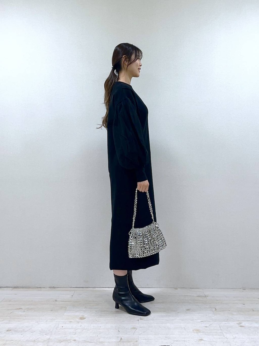 ブラック系のブーツ、ブラック系のワンピース、シルバー系のショルダーバッグを着用したレディースの冬コーディネートの2枚目の写真