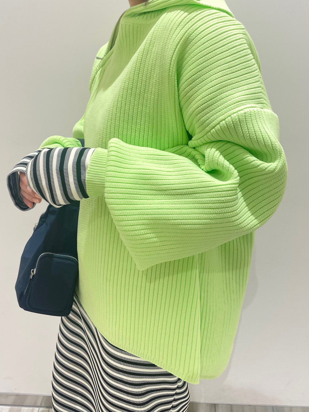 グリーン系のニット/セーター、ブラック系のワンピース、ブルー系のハンドバッグを着用したレディースの春コーディネートの3枚目の写真