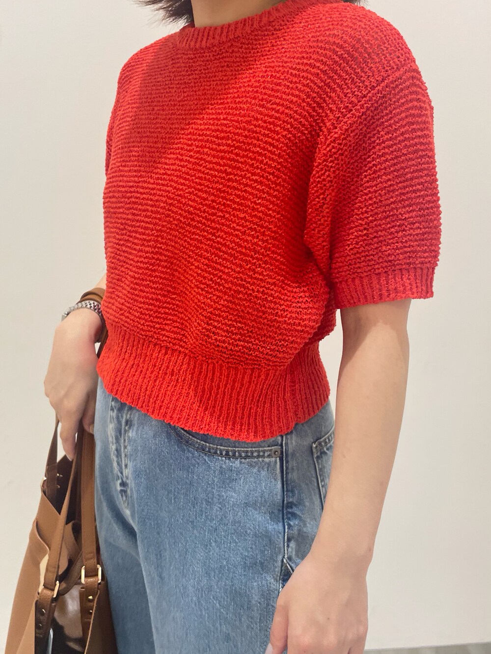 レッド系のニット/セーター、ブルー系のデニムパンツ、イエロー系のトートバッグを着用したレディースの春コーディネートの2枚目の写真