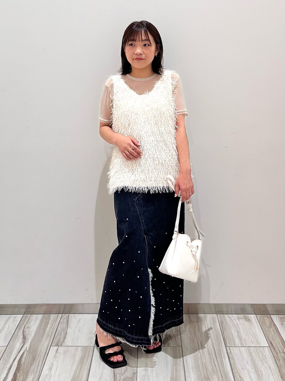 グレー系のタンクトップ、ブラック系のデニムスカート、ホワイト系のショルダーバッグを着用したレディースの夏コーディネートの2枚目の写真