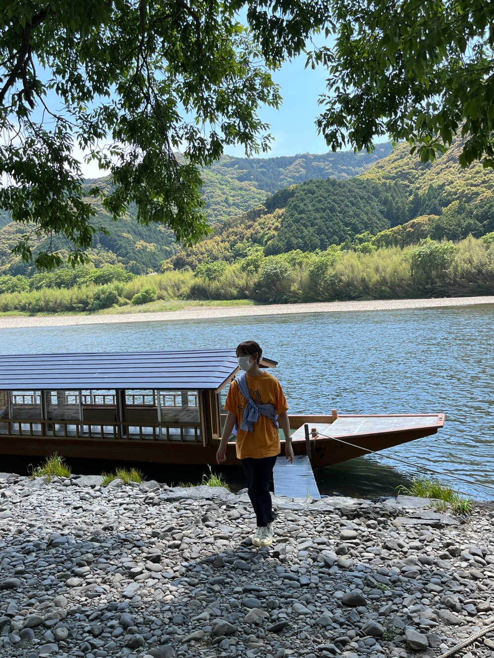ブルー系のシャツ/ブラウス、オレンジ系のTシャツ/カットソー、ブラック系のスカートを着用したレディースの春コーディネートの2枚目の写真