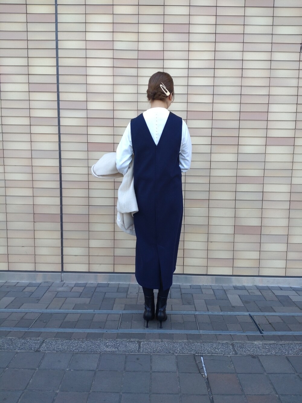 ベージュ系のハンドバッグ、ブラック系のブーツ、ブルー系のジャンパースカートを着用したレディースの冬コーディネートの2枚目の写真