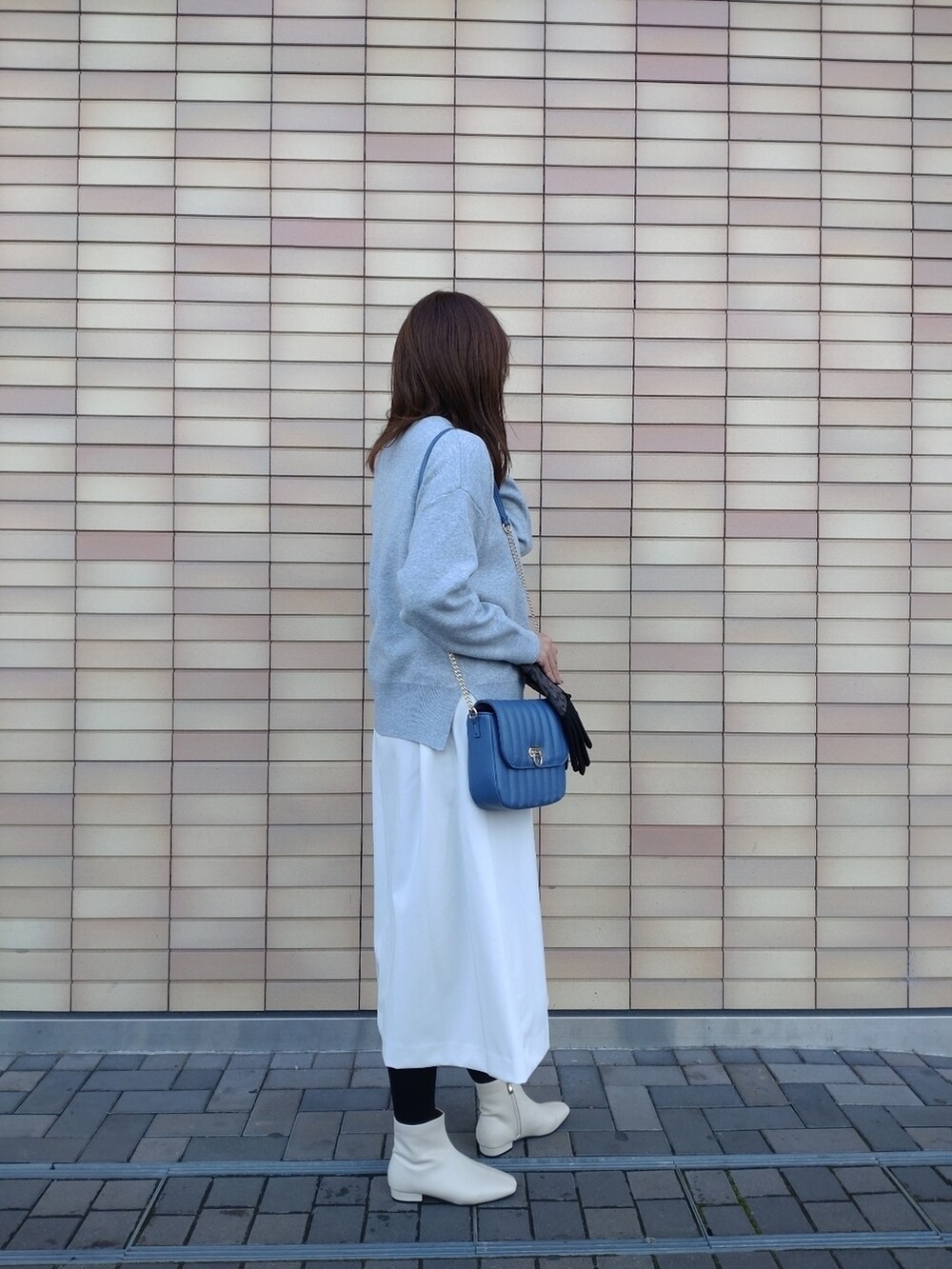 グレー系のニット/セーター、ホワイト系のスカート、ホワイト系のブーツを着用したレディースの冬コーディネートの2枚目の写真