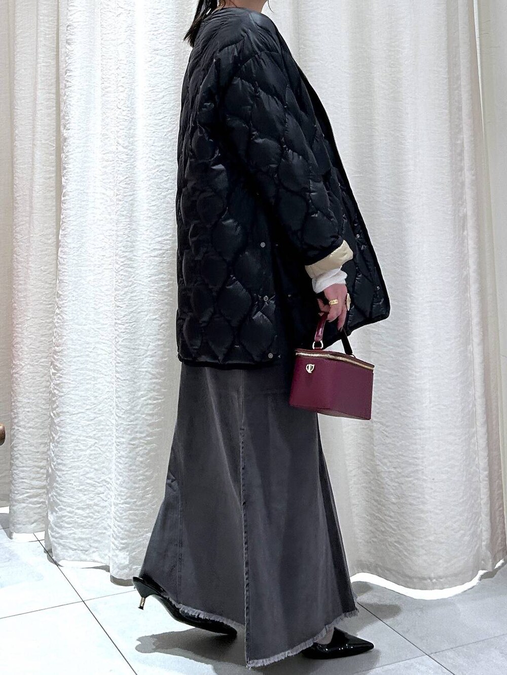 ブラック系のダウンジャケット/コート、グレー系のスカート、ホワイト系のニット/セーターを着用したレディースの秋コーディネートの6枚目の写真