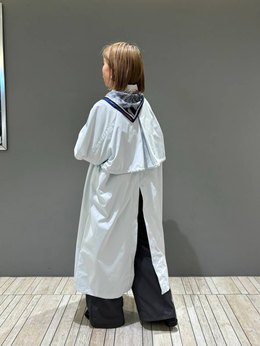 グレー系のスラックス、ブルー系のステンカラーコート、イエロー系のバンダナ/スカーフを着用したレディースの冬コーディネートの4枚目の写真