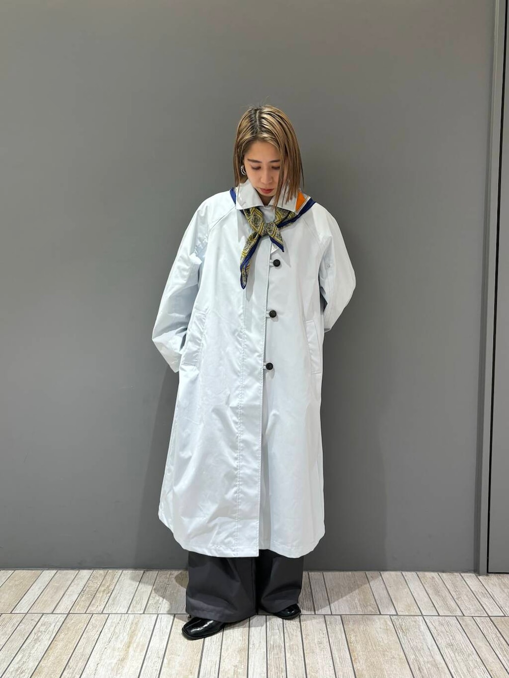 グレー系のスラックス、ブルー系のステンカラーコート、イエロー系のバンダナ/スカーフを着用したレディースの冬コーディネートの3枚目の写真