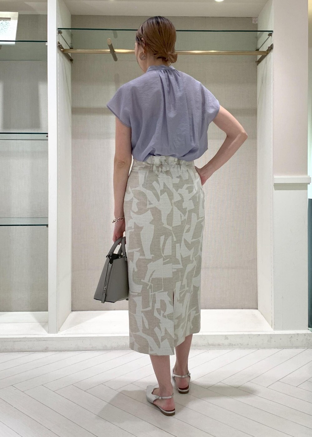 グレー系のハンドバッグ、シルバー系のパンプス、ベージュ系のスカートを着用したレディースの夏コーディネートの3枚目の写真
