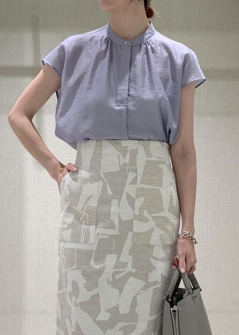 グレー系のハンドバッグ、シルバー系のパンプス、ベージュ系のスカートを着用したレディースの夏コーディネートの4枚目の写真