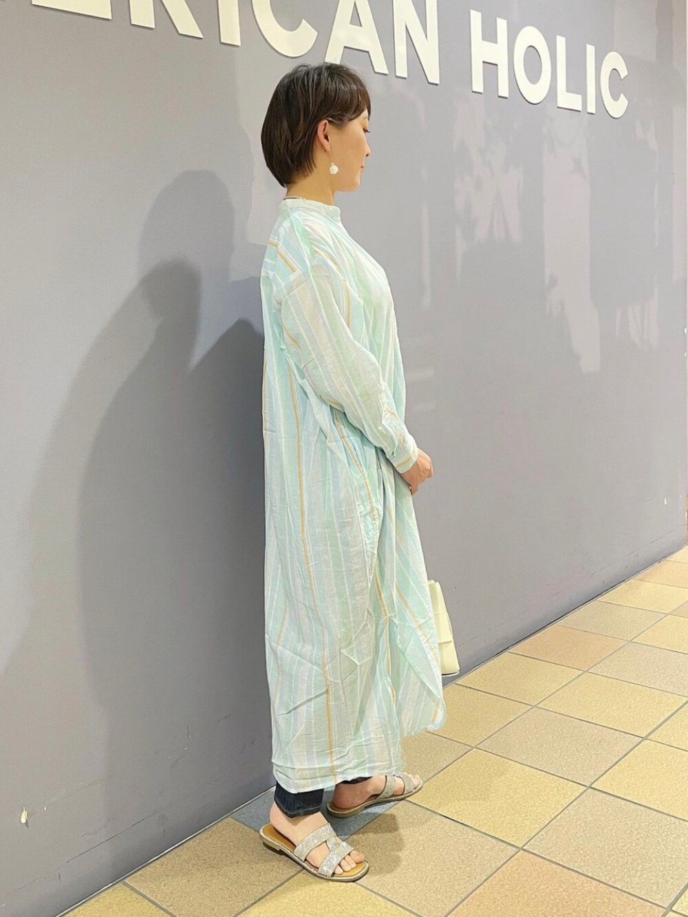 ホワイト系のショルダーバッグ、ブルー系のデニムパンツ、ブルー系のワンピースを着用したレディースの春コーディネートの3枚目の写真