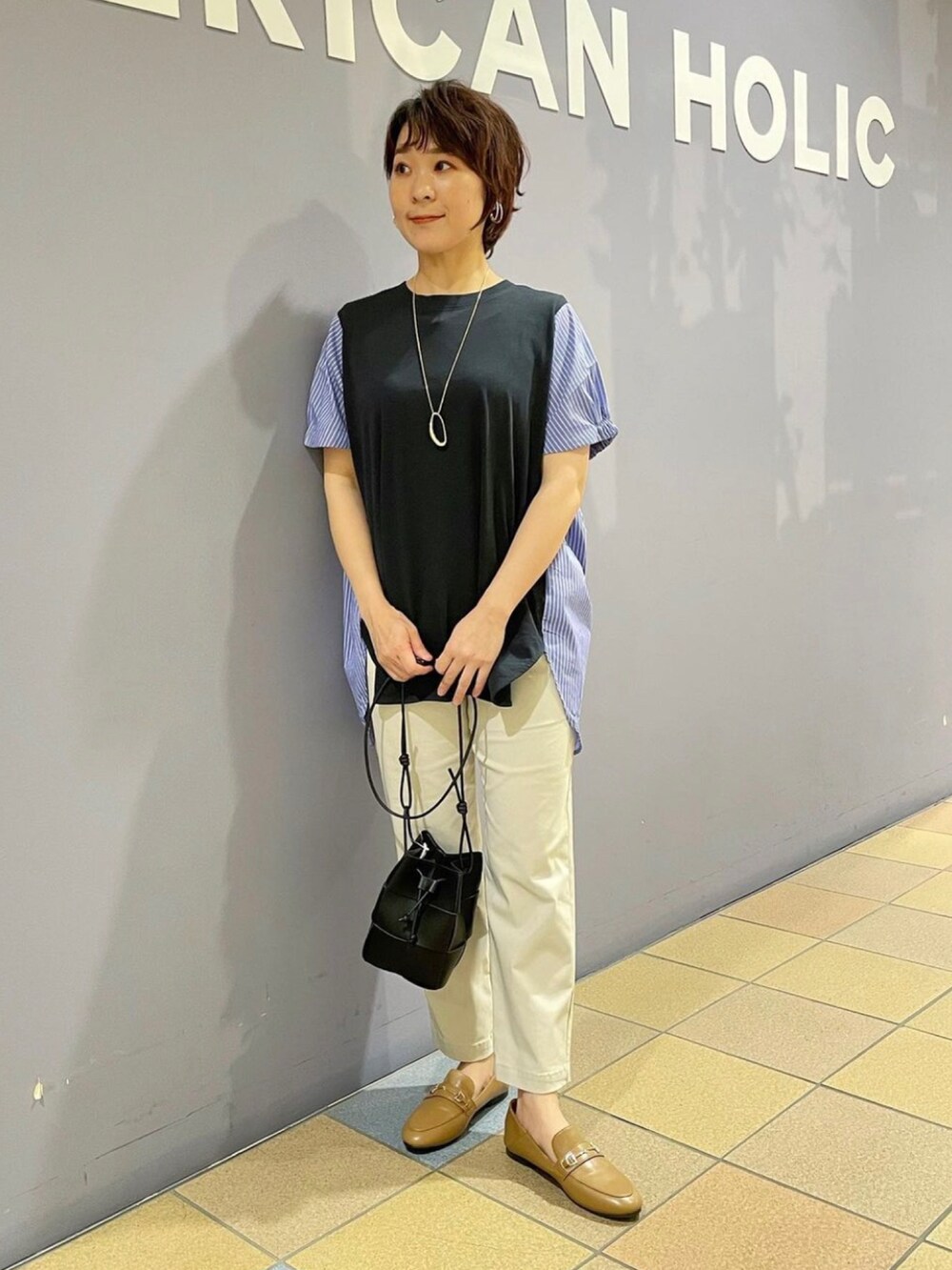 イエロー系のローファー、グレー系のその他パンツ、ブラック系のショルダーバッグを着用したレディースの夏コーディネートの2枚目の写真