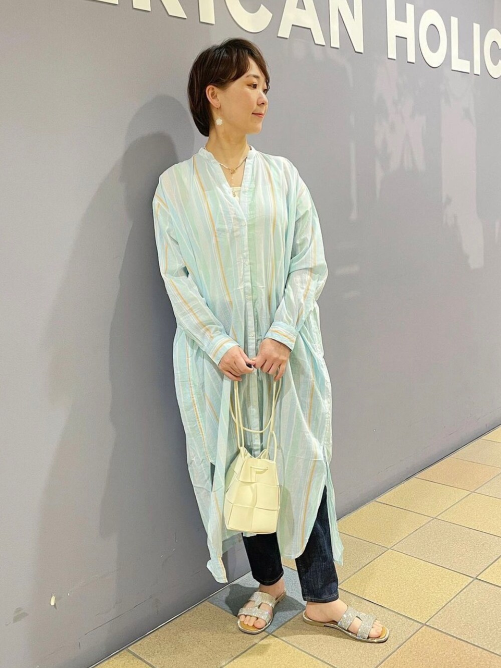 ホワイト系のショルダーバッグ、ブルー系のデニムパンツ、ブルー系のワンピースを着用したレディースの春コーディネートの5枚目の写真