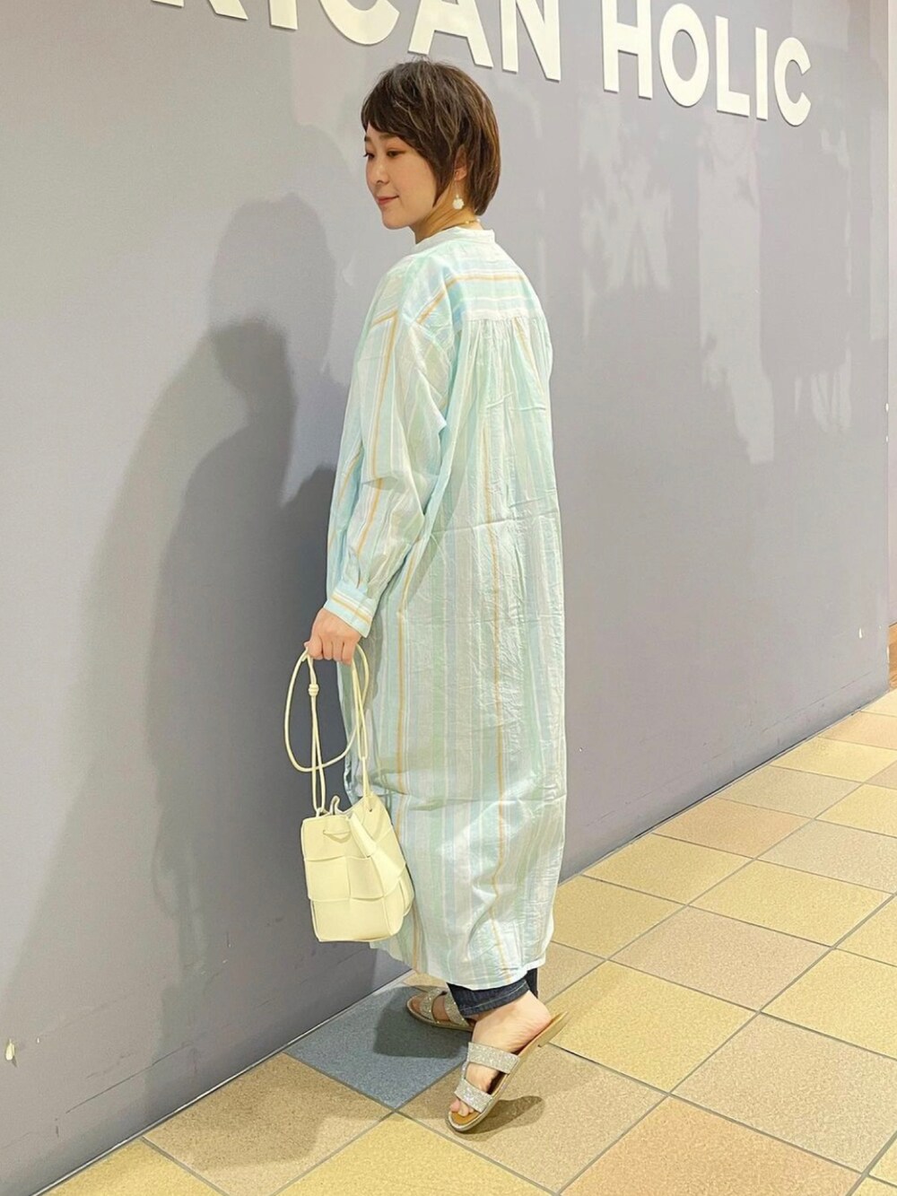 ホワイト系のショルダーバッグ、ブルー系のデニムパンツ、ブルー系のワンピースを着用したレディースの春コーディネートの2枚目の写真