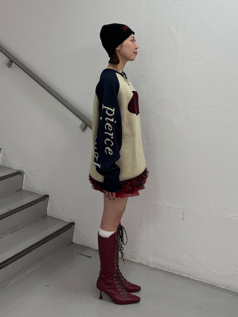 レッド系のブーツ、レッド系のスカート、ホワイト系のニット/セーターを着用したレディースの秋コーディネートの3枚目の写真