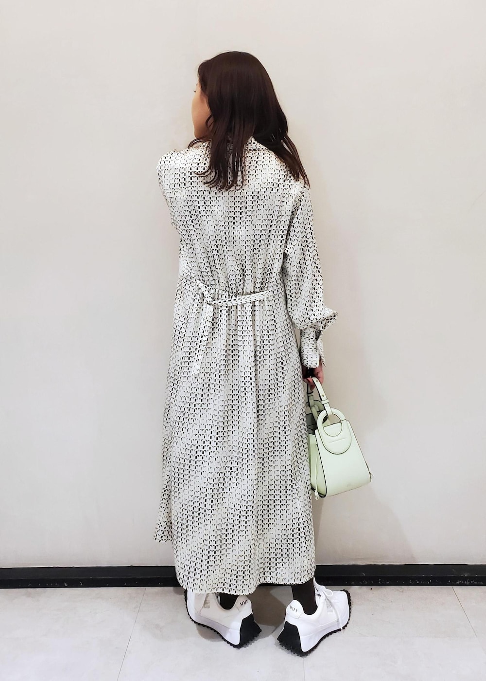 グリーン系のハンドバッグ、ホワイト系のスニーカー、ホワイト系のワンピースを着用したレディースの冬コーディネートの3枚目の写真