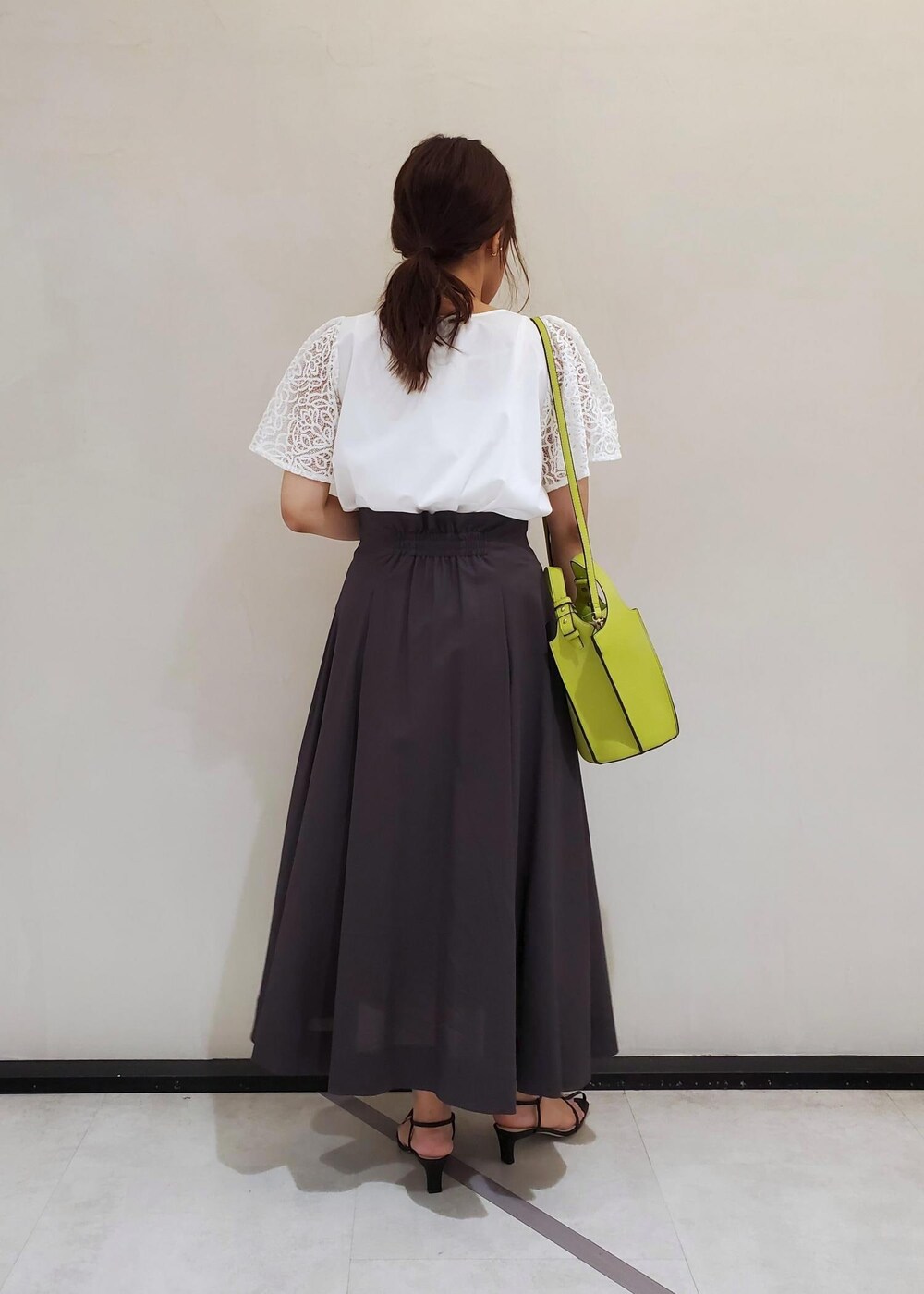 グリーン系のハンドバッグ、ブラック系のサンダル、ブラウン系のスカートを着用したレディースの夏コーディネートの3枚目の写真