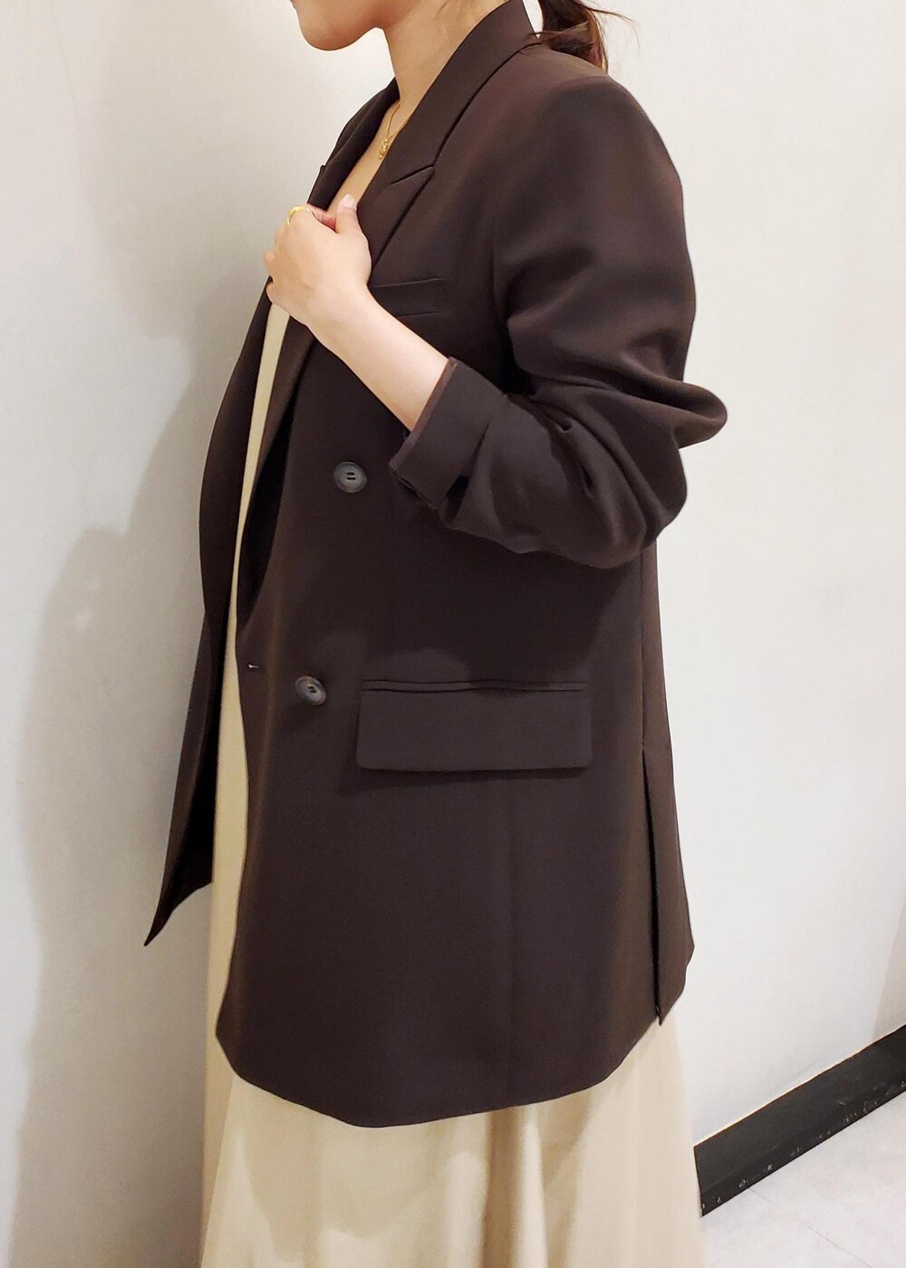 ブラウン系のテーラードジャケット、ベージュ系のワンピース、ゴールド系のネックレスを着用したレディースの春コーディネートの6枚目の写真