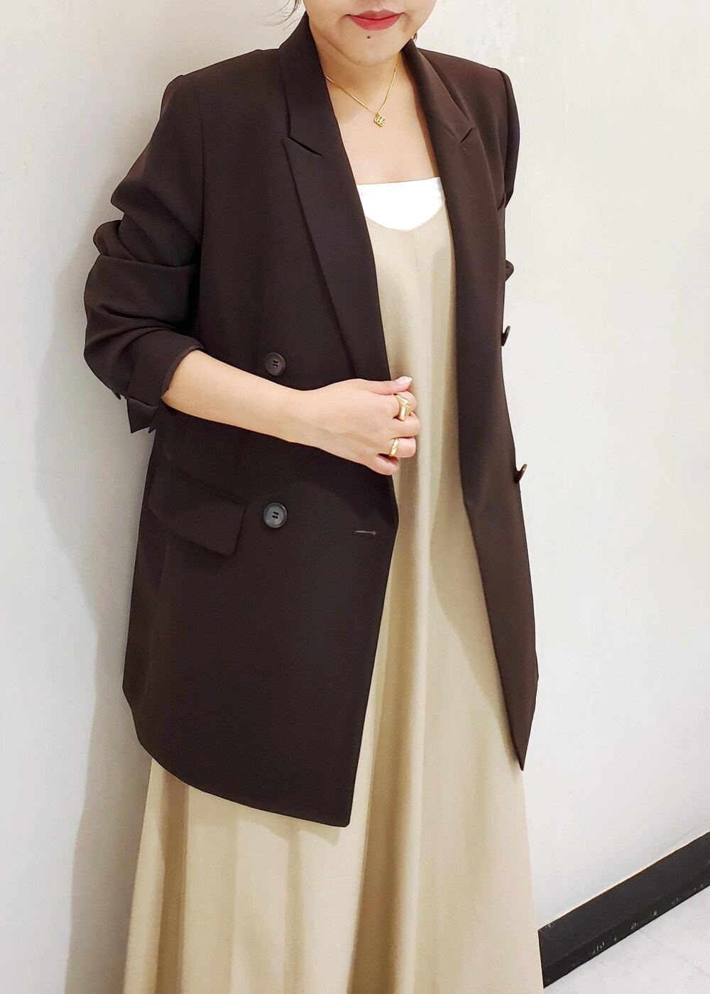 ブラウン系のテーラードジャケット、ベージュ系のワンピース、ゴールド系のネックレスを着用したレディースの春コーディネートの4枚目の写真