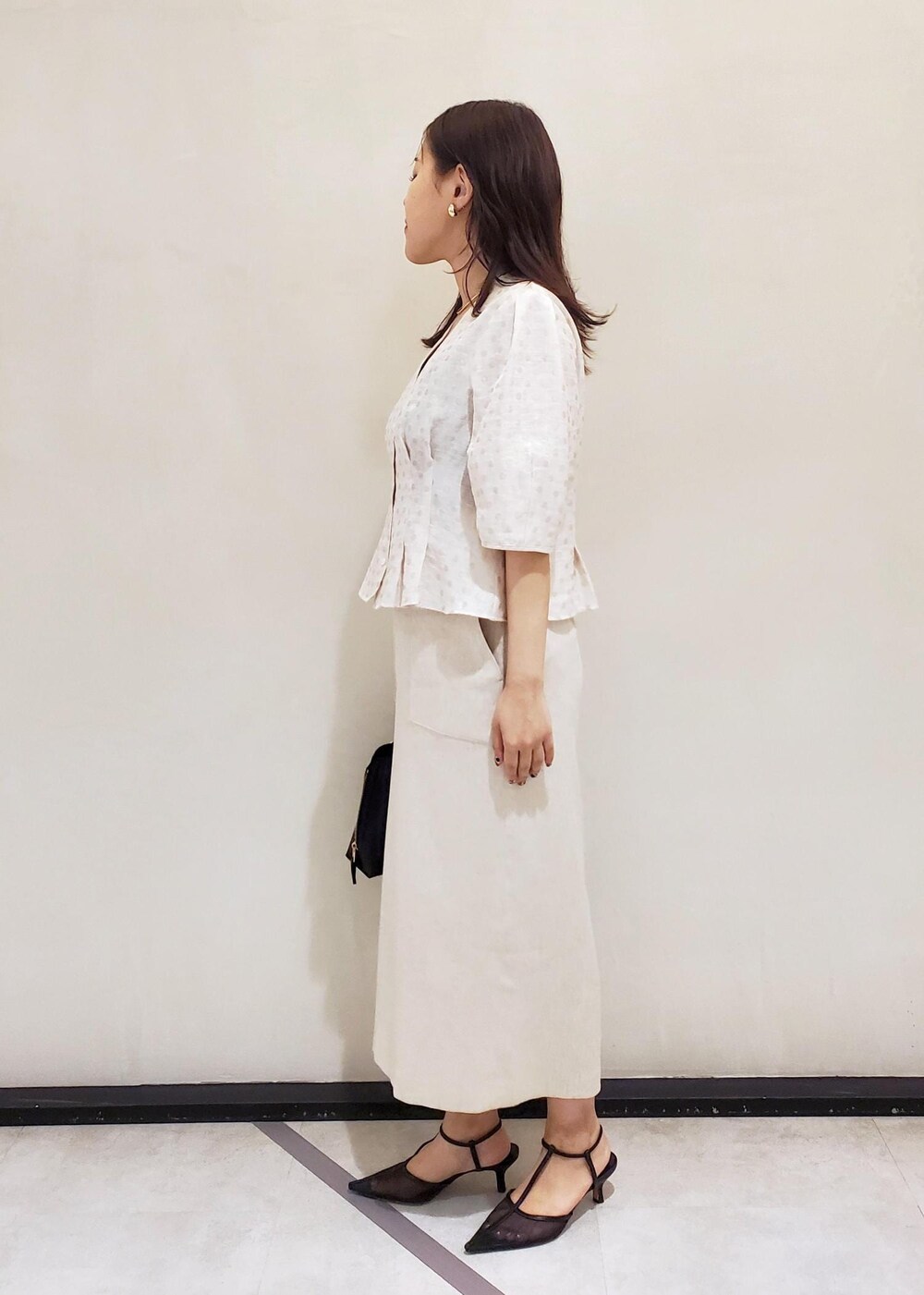 ブラック系のハンドバッグ、ブラック系のパンプス、ホワイト系のスカートを着用したレディースの夏コーディネートの2枚目の写真