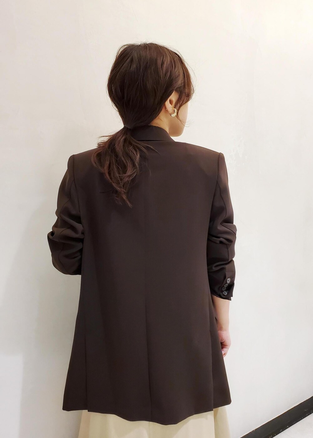 ブラウン系のテーラードジャケット、ベージュ系のワンピース、ゴールド系のネックレスを着用したレディースの春コーディネートの5枚目の写真