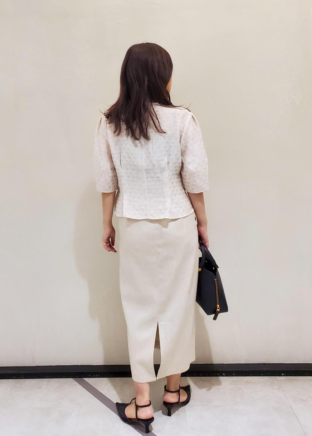 ブラック系のハンドバッグ、ブラック系のパンプス、ホワイト系のスカートを着用したレディースの夏コーディネートの3枚目の写真