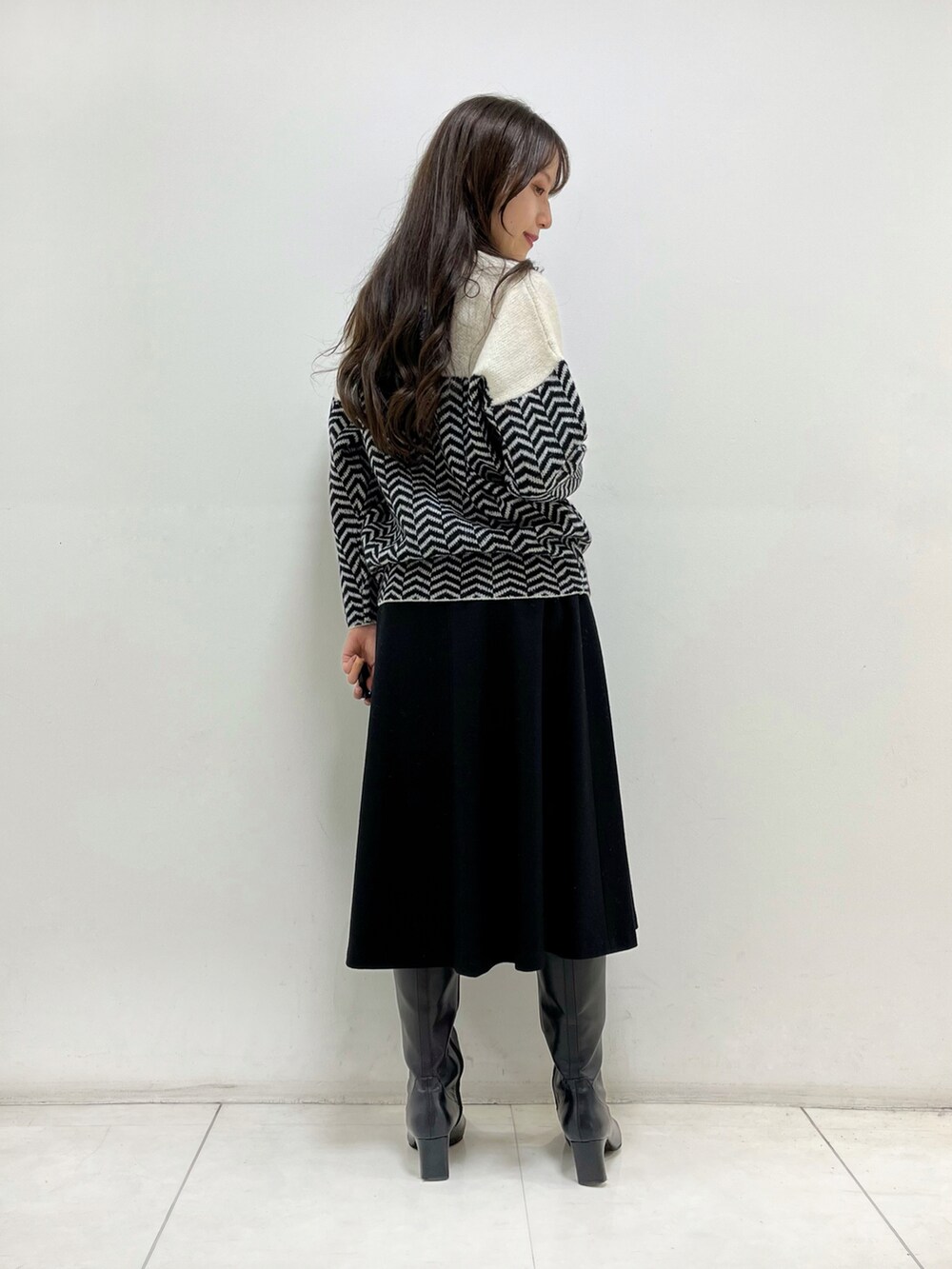 ホワイト系のニット/セーター、ブラック系のスカート、ブラック系のブーツを着用したレディースの秋コーディネートの5枚目の写真