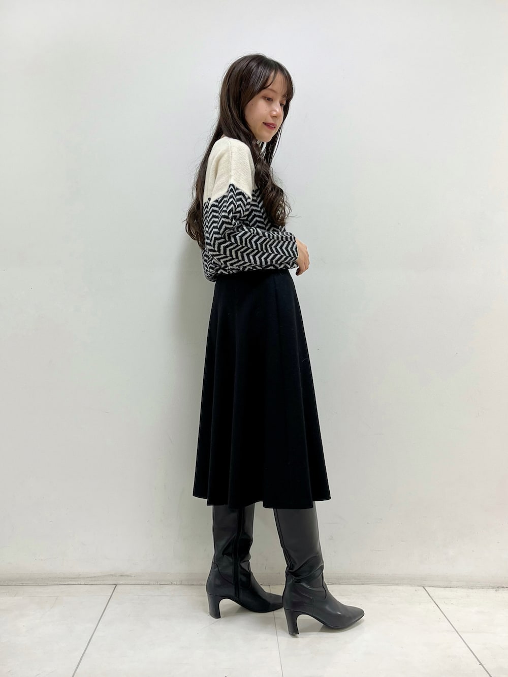 ホワイト系のニット/セーター、ブラック系のスカート、ブラック系のブーツを着用したレディースの秋コーディネートの2枚目の写真