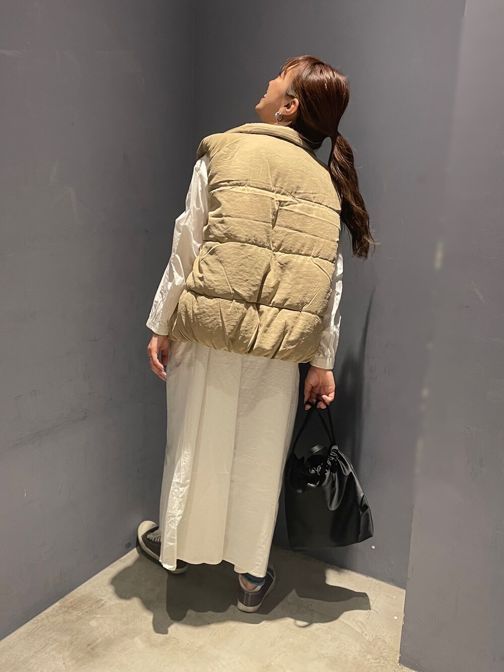 ベージュ系のダウンベスト、ホワイト系のワンピース、ブラック系のショルダーバッグを着用したレディースの秋コーディネートの2枚目の写真