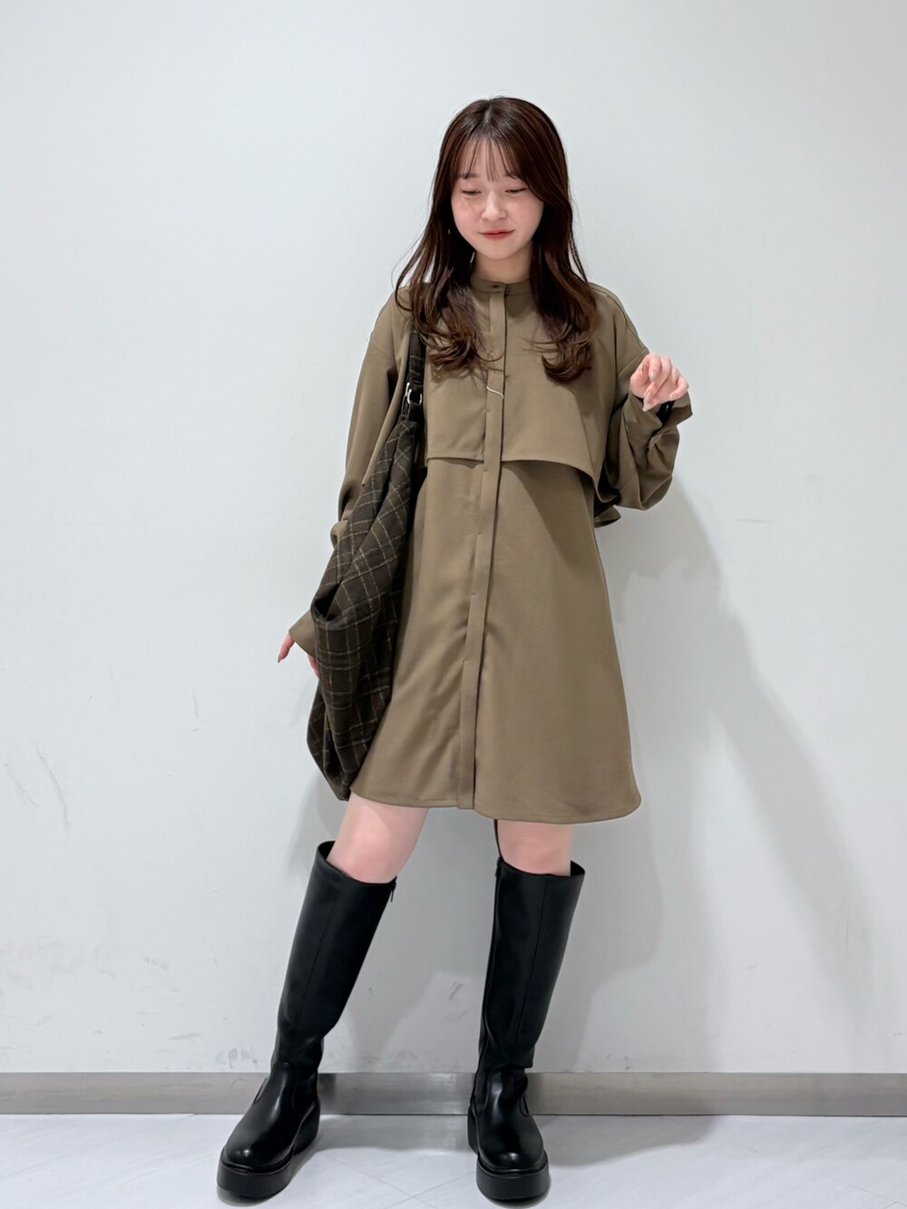 ブラック系のステンカラーコート、ブラウン系のワンピース、ブラック系のブーツを着用したレディースの秋コーディネートの4枚目の写真