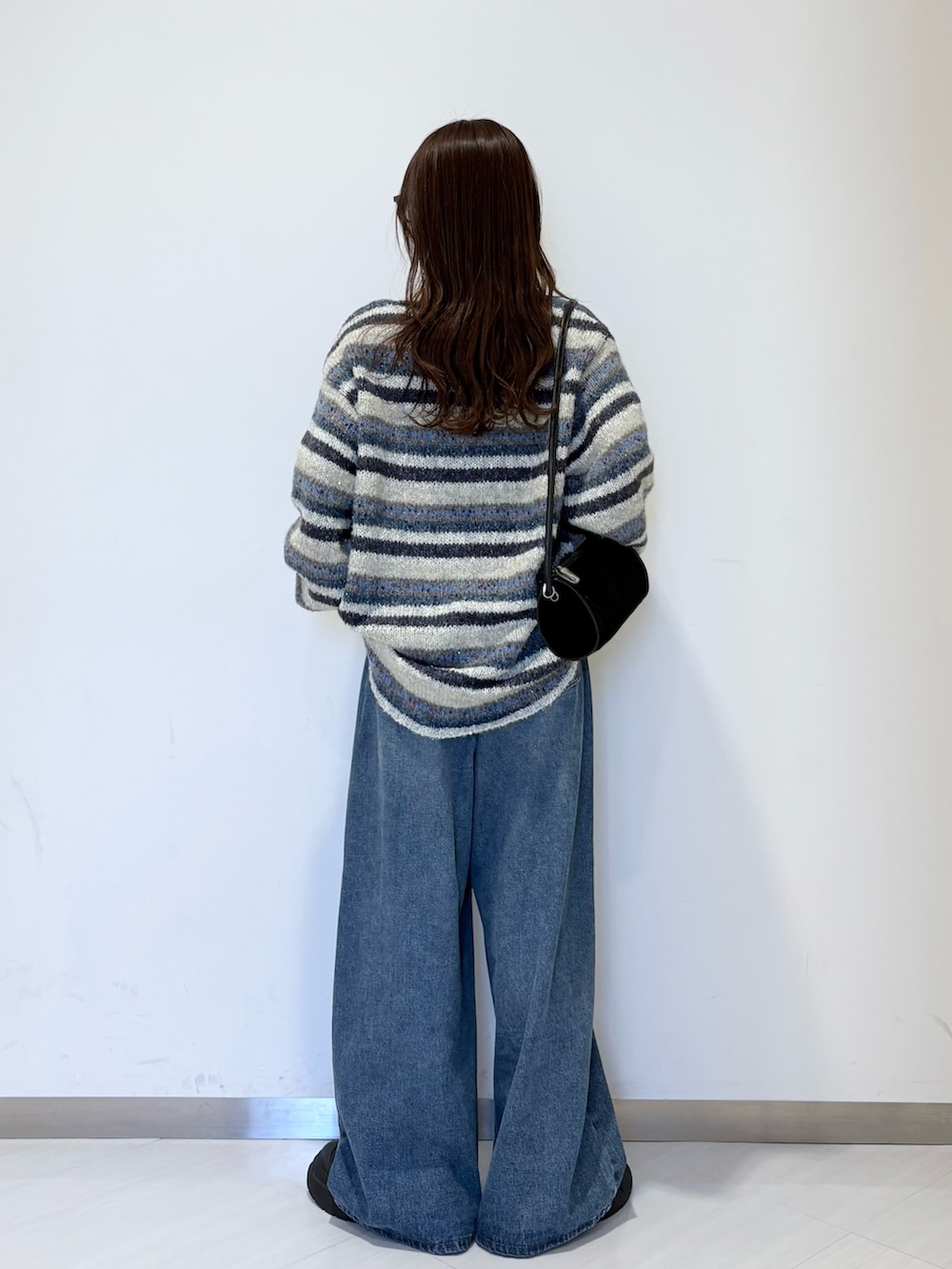 ブルー系のニット/セーター、ブルー系のデニムパンツ、ブラック系のショルダーバッグを着用したレディースの秋コーディネートの2枚目の写真