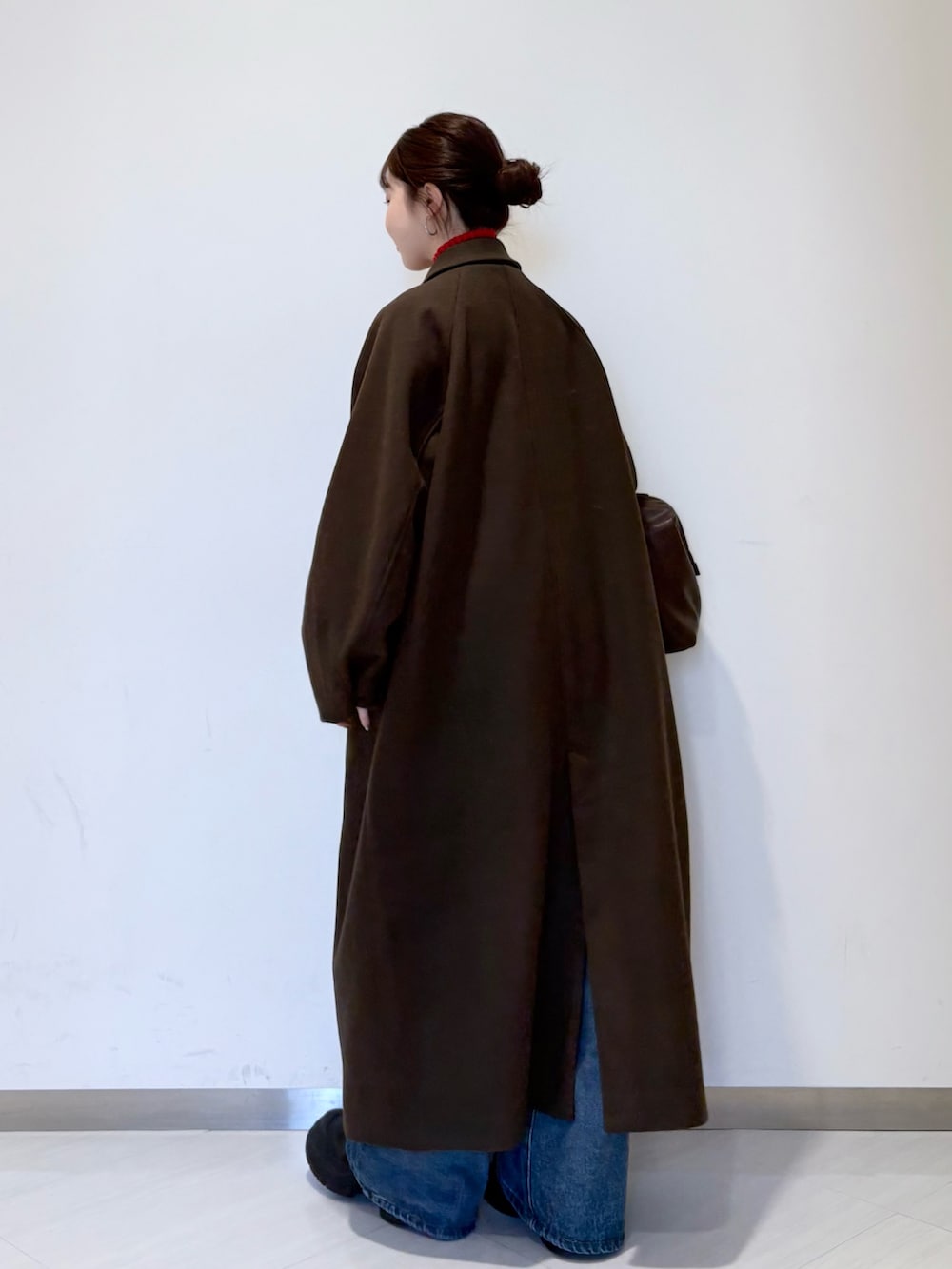 レッド系のニット/セーター、ブラウン系のステンカラーコート、ブルー系のデニムパンツを着用したレディースの秋コーディネートの3枚目の写真