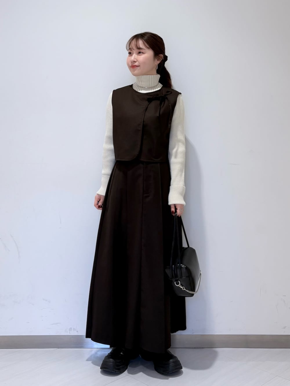 ブラック系のショルダーバッグ、ブラウン系のワンピース、ホワイト系のニット/セーターを着用したレディースの冬コーディネートの2枚目の写真